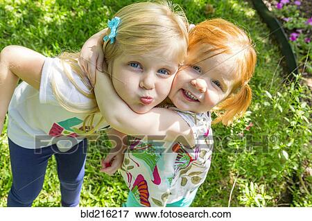 Stock Photo - Caucasian sisters hugging in backyard. Fotosearch