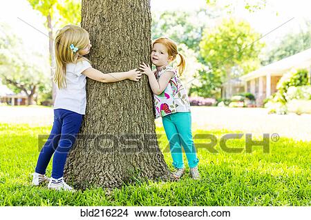 Picture - Caucasian sisters hugging tree in backyard. Fotosearch