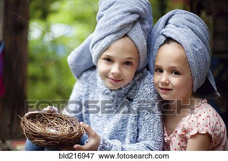 Stock Photo - Caucasian sisters in hair towels holding bird nest. Fotosearch