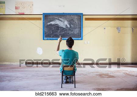 Stock Image - Caucasian student sitting in empty classroom. Fotosearch