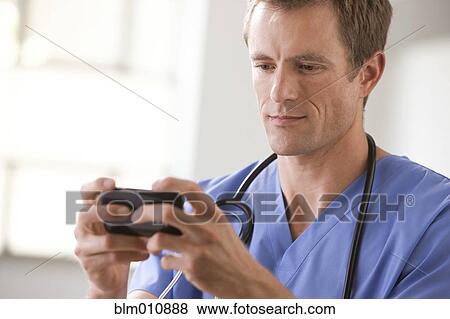 Stock Photo - Caucasian surgeon text messaging on cell phone. Fotosearch