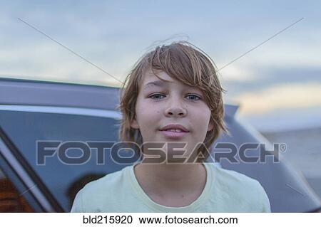 Stock Image - Caucasian teenage boy smiling at car. Fotosearch