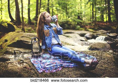 Stock Photograph - Caucasian teenage girl drinking coffee on forest rock. Fotosearch