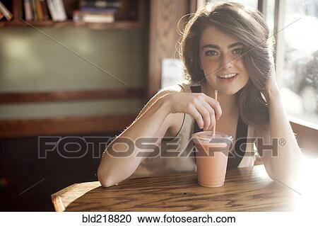 Stock Image - Caucasian teenage girl drinking smoothie in cafe. Fotosearch