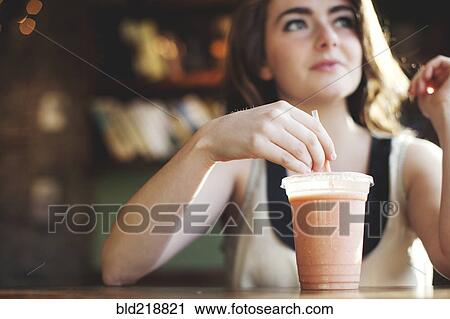 Stock Image - Caucasian teenage girl drinking smoothie in cafe. Fotosearch