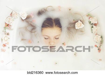 Stock Image - Caucasian teenage girl floating in milk bath with flowers. Fotosearch