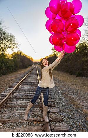 Caucasian teenage girl holding bunch of balloons on train tracks View Large Photo Image Stock Image - Caucasian teenage girl holding bunch of balloons on train tracks. Fotosearch