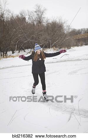 Stock Image - Caucasian teenage girl ice skating on frozen lake. Fotosearch