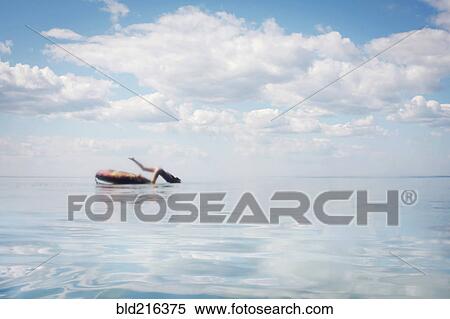 Stock Photography - Caucasian teenage girl jumping from inner tube into lake. Fotosearch