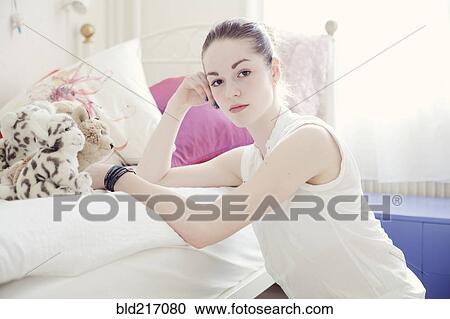 Stock Image - Caucasian teenage girl leaning on bed. Fotosearch
