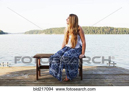 Picture - Caucasian teenage girl sitting on wooden dock at lake. Fotosearch