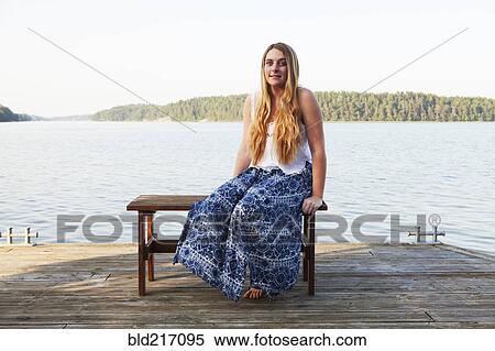 Stock Photography - Caucasian teenage girl sitting on wooden dock at lake. Fotosearch
