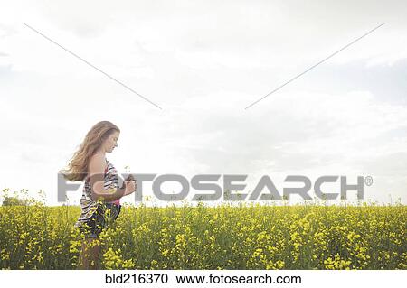 Stock Image - Caucasian teenage girl standing in field of flowers. Fotosearch
