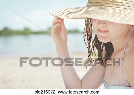 Stock Image - Caucasian teenage girl wearing sun hat on beach. Fotosearch