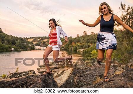 Stock Image - Caucasian teenage girls running on riverbank. Fotosearch