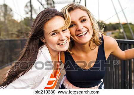 Stock Image - Caucasian teenage girls smiling on wooden bridge. Fotosearch