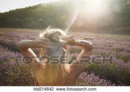 Stock Image - Caucasian woman admiring field of flowers. Fotosearch