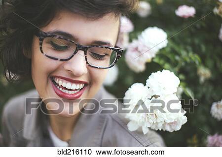 Stock Image - Caucasian woman admiring flowers on shrub. Fotosearch