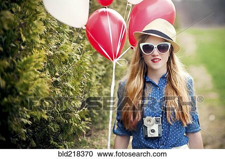 Stock Image - Caucasian woman carrying balloons and instant camera. Fotosearch