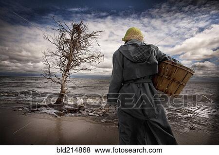 Stock Photo - Caucasian woman carrying basket on windy beach. Fotosearch