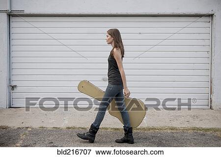 Stock Photo - Caucasian woman carrying guitar case on sidewalk. Fotosearch