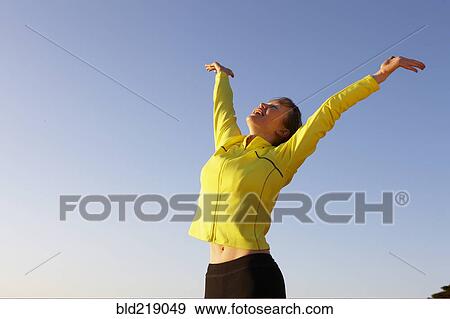 Stock Photo - Caucasian woman cheering with arms outstretched under blue sky. Fotosearch