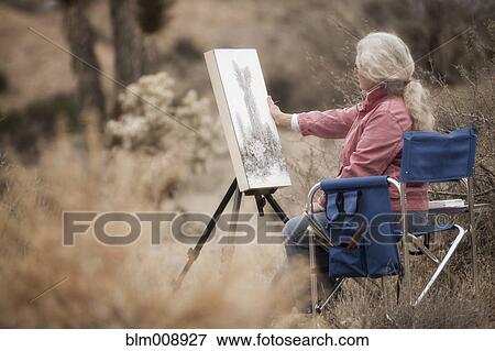 Stock Photo - Caucasian woman drawing on easel outdoors. Fotosearch