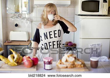 Picture - Caucasian woman drinking coffee in kitchen. Fotosearch
