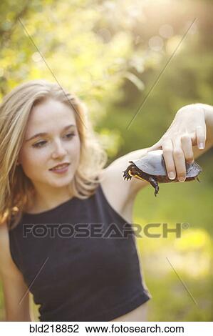 Stock Image - Caucasian woman examining turtle in forest. Fotosearch