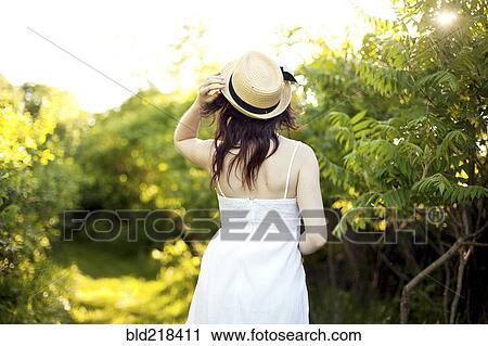 Stock Image - Caucasian woman holding hat on rural path. Fotosearch