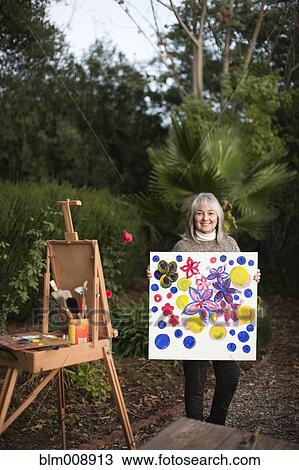 Stock Image - Caucasian woman holding painting outdoors. Fotosearch