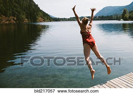 Stock Photo - Caucasian woman jumping from dock into rural lake. Fotosearch