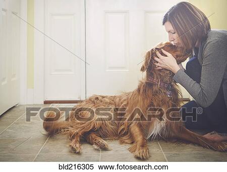 Stock Photography - Caucasian woman kissing dog on floor. Fotosearch