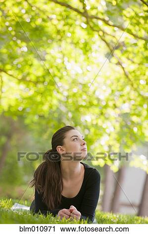 Stock Image - Caucasian woman laying in grass in park. Fotosearch