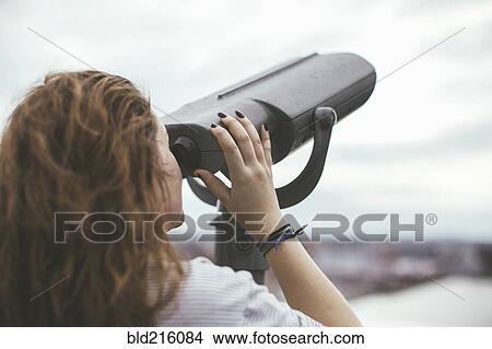 Picture - Caucasian woman on urban rooftop admiring cityscape with telescope. Fotosearch