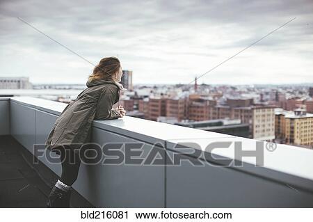 Stock Image - Caucasian woman on urban rooftop admiring cityscape. Fotosearch