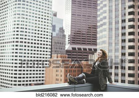 Stock Image - Caucasian woman on urban rooftop admiring cityscape. Fotosearch