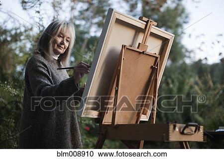 Stock Image - Caucasian woman painting on easel outdoors. Fotosearch