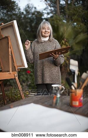 Stock Image - Caucasian woman painting on easel outdoors. Fotosearch