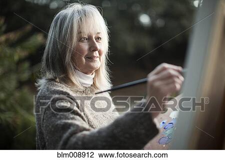 Stock Image - Caucasian woman painting on easel outdoors. Fotosearch