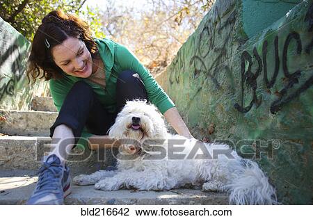 Stock Image - Caucasian woman petting dog on staircase with graffiti. Fotosearch