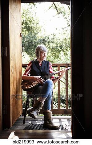 Stock Image - Caucasian woman playing guitar on porch. Fotosearch