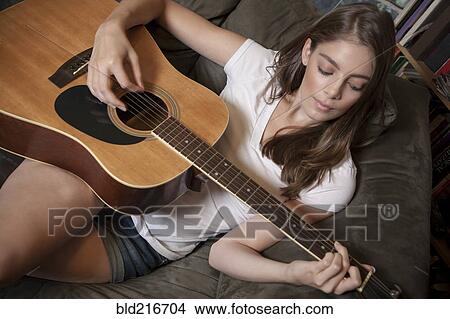 Picture - Caucasian woman playing guitar on sofa. Fotosearch