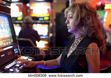 Stock Photo - Caucasian woman playing slot machine in casino. Fotosearch