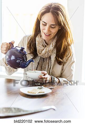 Stock Image - Caucasian woman pouring cup of tea at table. Fotosearch