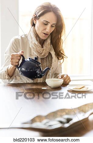 Stock Image - Caucasian woman pouring cup of tea at table. Fotosearch