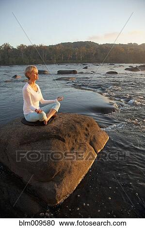 Stock Image - Caucasian woman practicing yoga on rock near ocean. Fotosearch