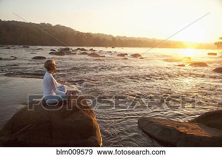 Stock Photo - Caucasian woman practicing yoga on rock near ocean. Fotosearch