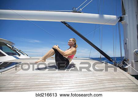 Stock Image - Caucasian woman practicing yoga on sailboat deck. Fotosearch