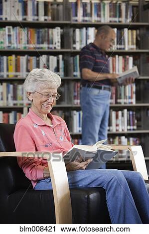 Stock Image - Caucasian woman reading book in library. Fotosearch